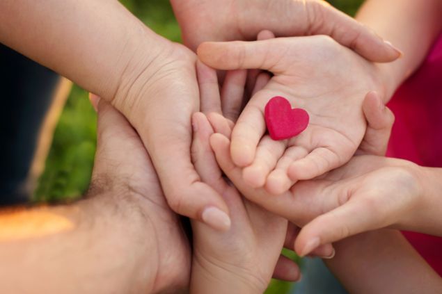 Imagem de várias mãos sobrepostas (mãe, pai e filho) e sobre a última mão, há um símbolo de um coração. A imagem representa a relação familiar.