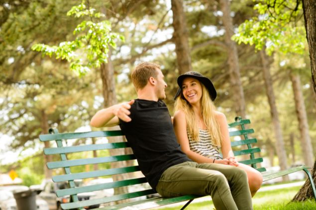 Imagem de uma praça e nela um casal de namorados sentados em banco conversando.