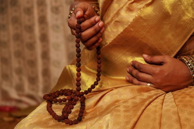 Imagem de uma pessoa usando uma roupa dourada e segurando em uma das mãos  uma guia de contas de oração para a Cabocla Jurema