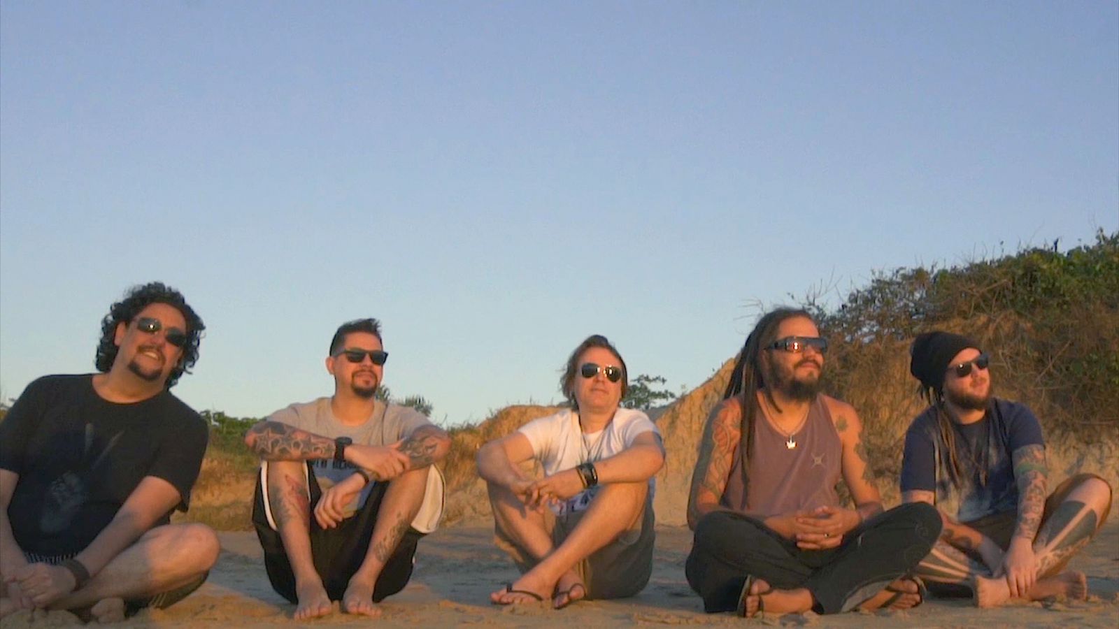 Membros da banda Maskavo sentados em uma praia.